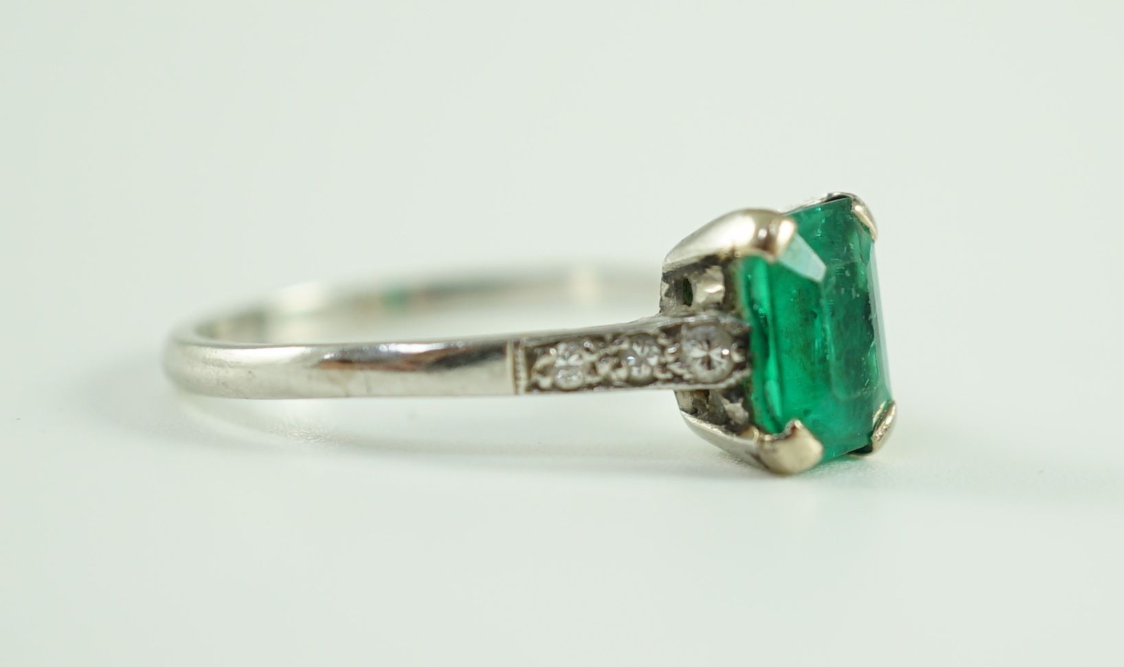 A white gold and single stone emerald ring, with six stone diamond set shoulders